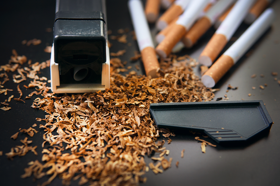 Stopfmaschine, loser Tabak und mehrere fertige Zigaretten auf dunkler Oberfläche in Nahaufnahme