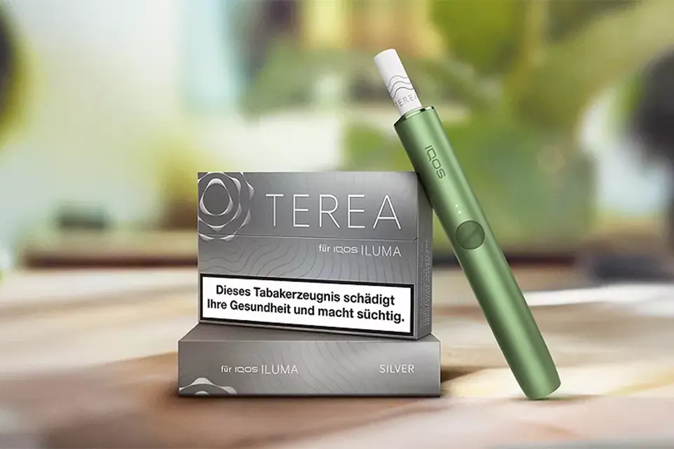 IQOS ILUMA Tabakerhitzer in Grün mit TEREA Silver Packung auf einem Tisch